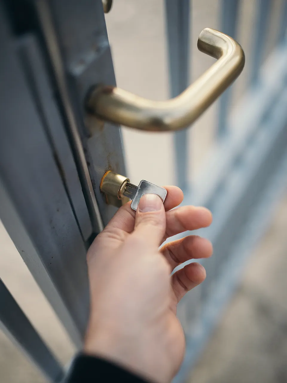 Hand dreht einen Schlüssel im Profilzylinder einer Tür mit Messingdrücker